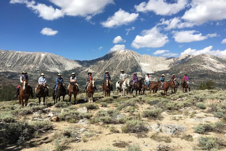 group of horseback riders on horses with mountains in background